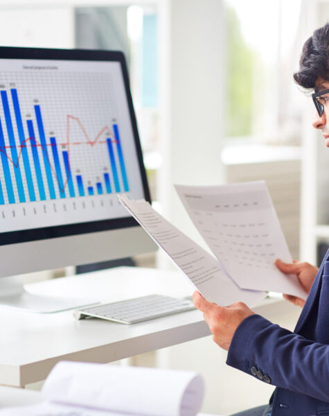 Businessman looking through papers by workplace and analyzing statistics