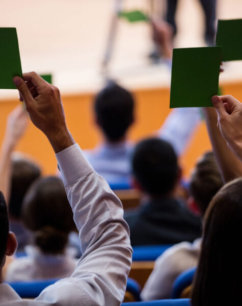 Rear view of business executives show their approval by raising hands at conference center