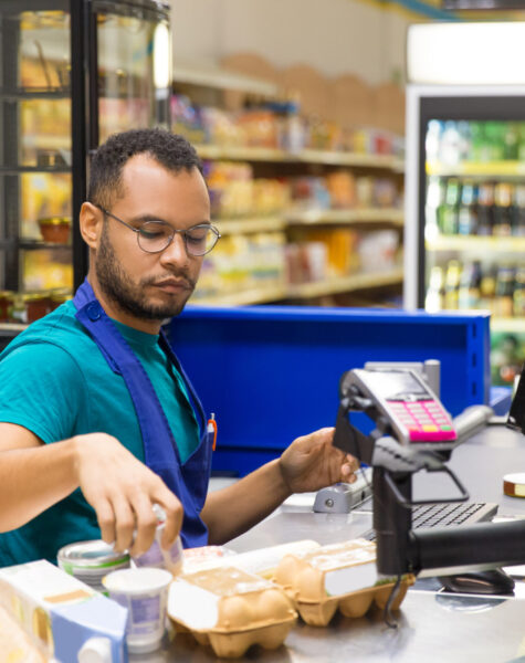 Focused African American cashier scanning goods at checkout. Concentrated young man in eyeglasses at workplace. Shopping concept